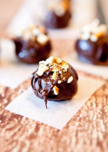 Chocolate truffle topped with crushed nuts on a white paper.