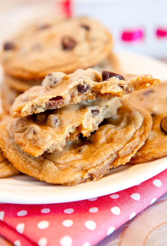 Snickers Bar Stuffed Chocolate Chip Cookies stacked om plate with one cookie split in half showing inside
