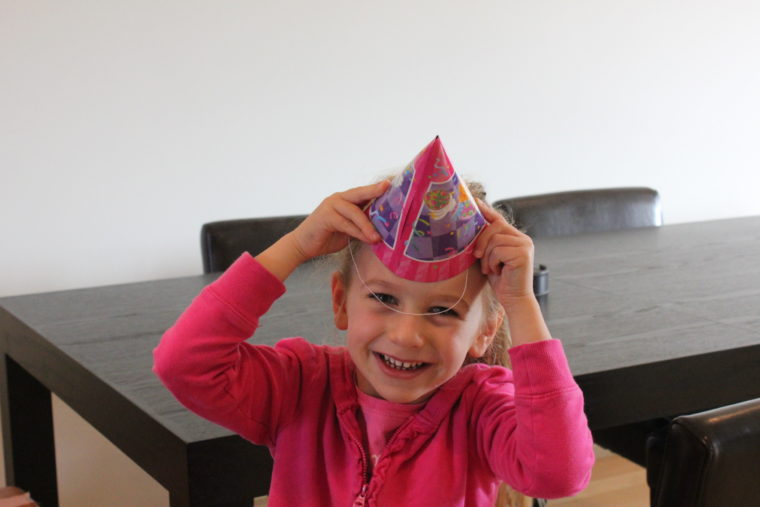 Young girl holding birthday hat to head and smiling