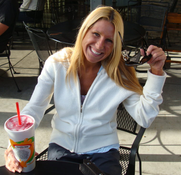 Woman sitting at outdoor table drinking a smoothie and smiling