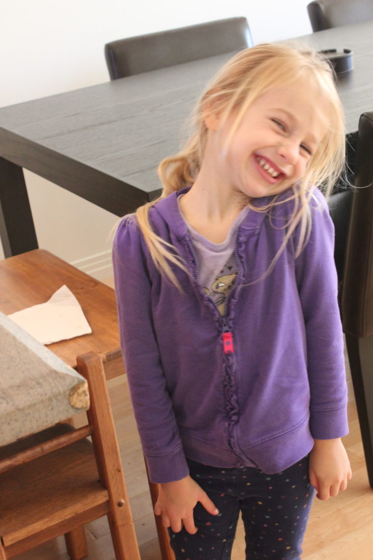 Young girl in purple zip up smiling with her head toward her shoulder