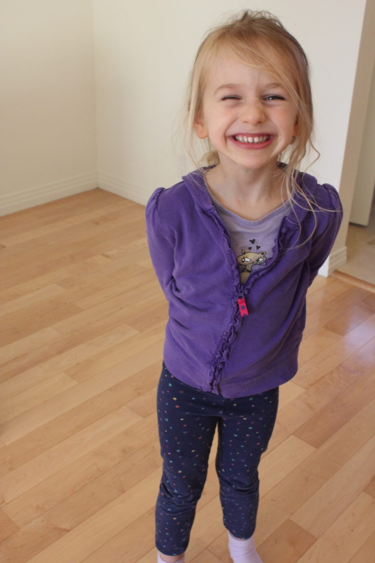 Young girl in purple smiling with hands behind back