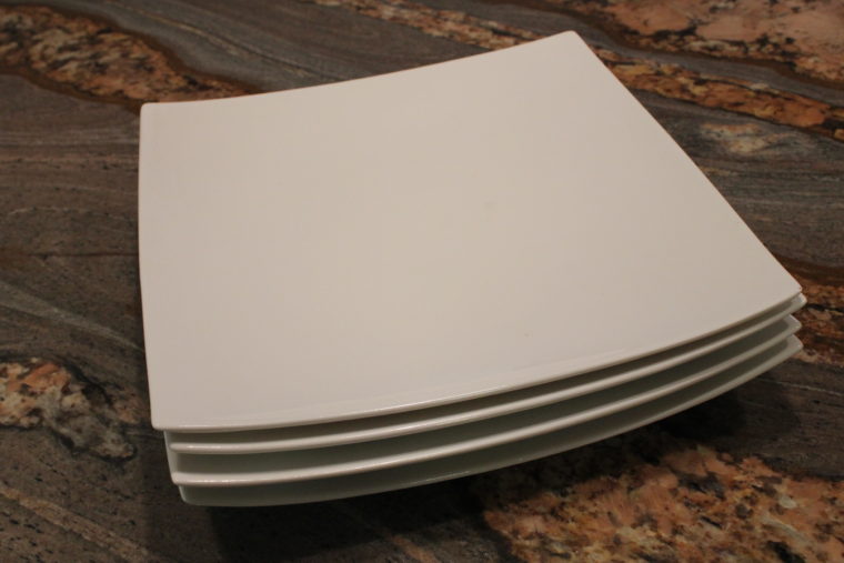 Four stacked white square plates