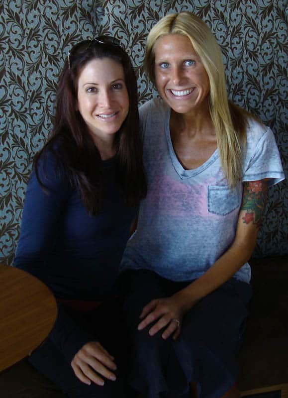 Two woman sitting with arms around one another smiling