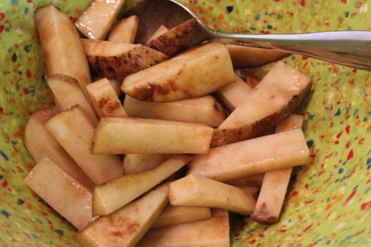 Ingredients for Cinnamon-Sugar and Ginger-Roasted Potato Sticks in bowl with spoon