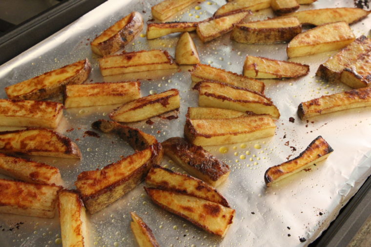 Cinnamon-Sugar and Ginger-Roasted Potato Sticks on pan after being flipped halfway through baking 