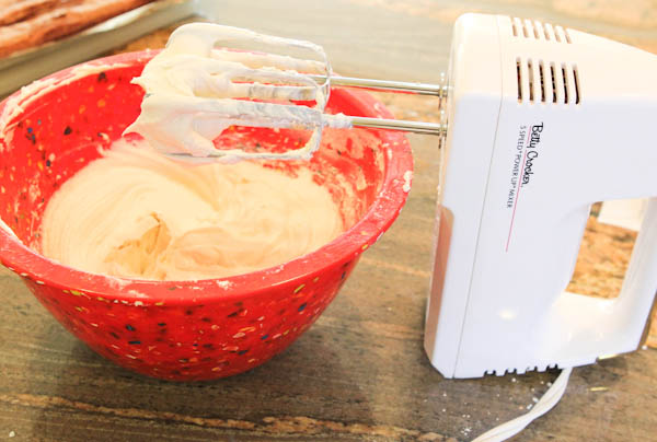 electric mixer mixing frosting in red bowl