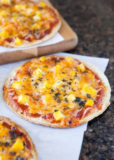 Homemade mini pizzas with cheese and diced toppings on a kitchen counter.