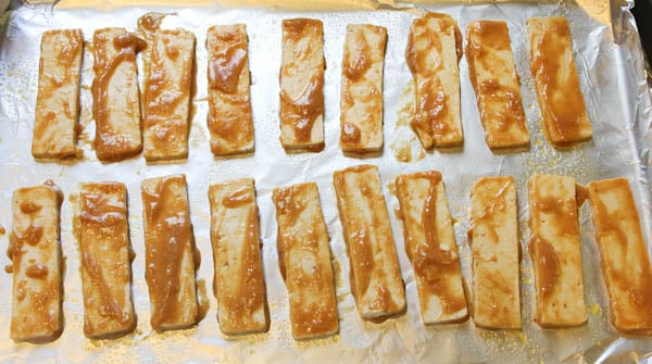 Slices of Tofu covered in Peanut Sauce on foiled lined baking sheet