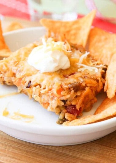 A plate of nachos topped with melted cheese, a scoop of sour cream, and a hearty meat and bean mixture.