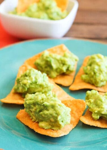 Corn chips topped with guacamole on a blue plate.