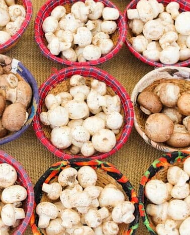 Various types of mushrooms displayed in baskets for sale.