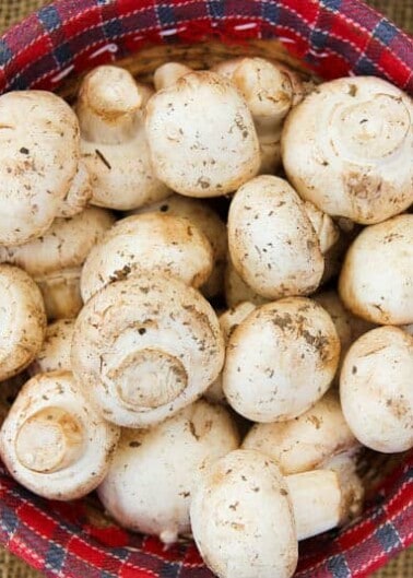 A basket of fresh, unwashed white mushrooms with visible soil.