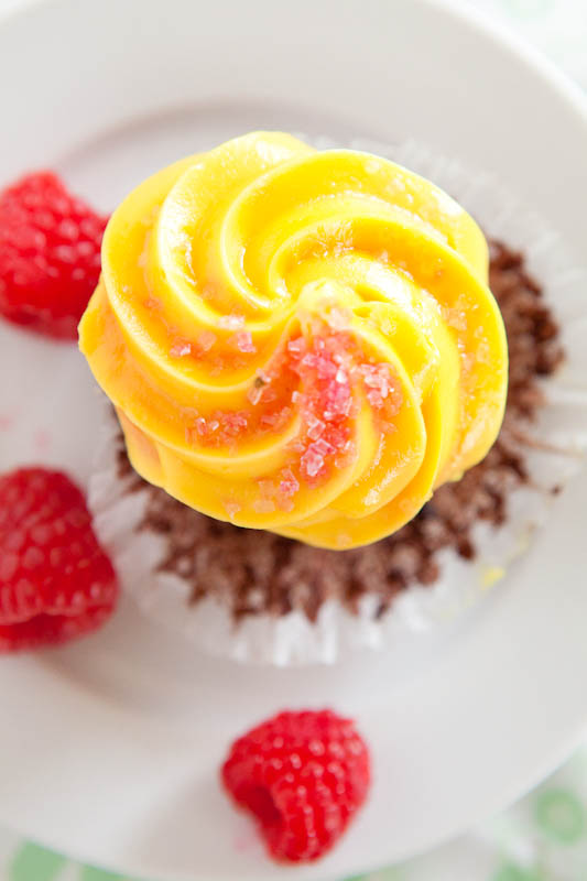 Cupcake with yellow frosting surrounded by rasperries