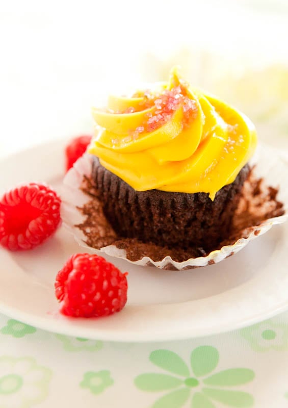 Chocolate cupcake with yellow frosting with raspberries on plate