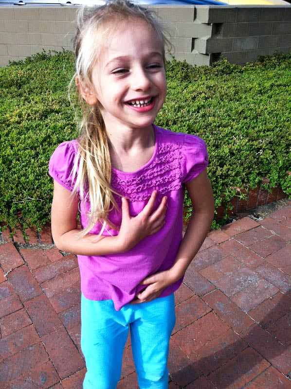 Young girl on sidewalk with hand to chest smiling