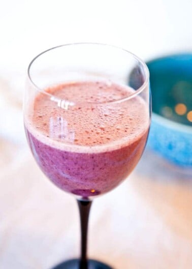 A close-up of a smoothie in a wine glass with a blurred background.