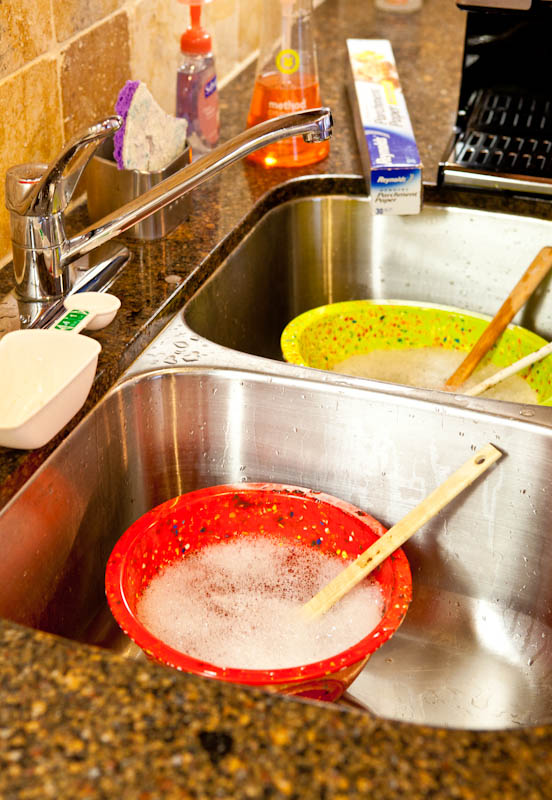 filled kitchen sink with red and yellow bowls with spatulas in them
