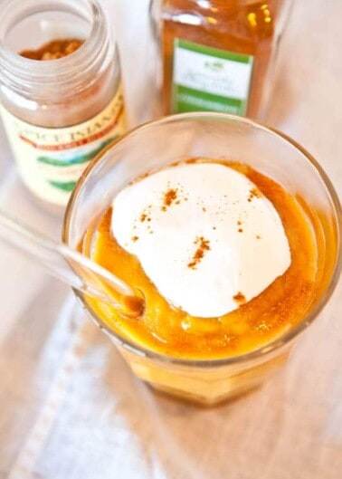 A dollop of cream on top of a pumpkin-flavored dessert, with spice jars in the background.