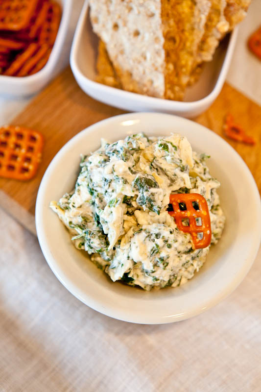 Spinach and Artichoke Dip in white bowl with pretzel dipped in