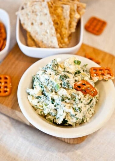 Bowl of spinach dip with assorted crackers and bread on a table.