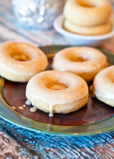 Glazed doughnuts on a plate with icing dripping off the sides.