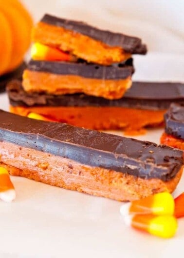 Chocolate-covered cookie bars with a pumpkin and candy corns in the background, suggesting a seasonal autumn treat.
