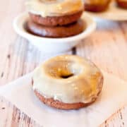 Glazed doughnuts on a wooden surface with more in the background.