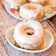 Glazed donuts on a small plate and in a bowl on a wooden surface.