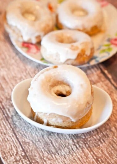 Glazed donuts on a small plate and in a bowl on a wooden surface.