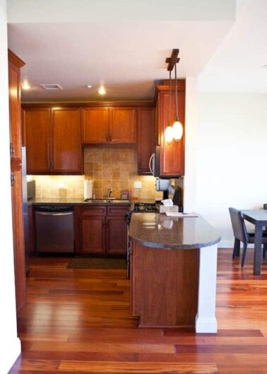 Modern kitchen interior with wooden cabinets, hardwood floors, and a curved breakfast bar.