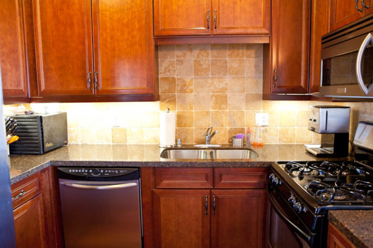 Mahogany kitchen with marble countertops and tile backsplash, stove and microwave on the right