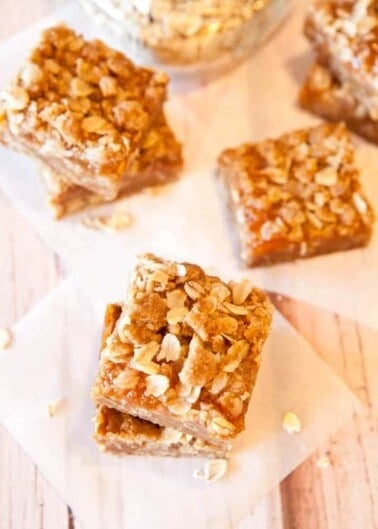 Homemade oatmeal bars on a wooden surface with rolled oats in the background.