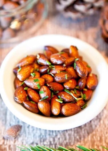 A bowl of roasted almonds garnished with herbs.
