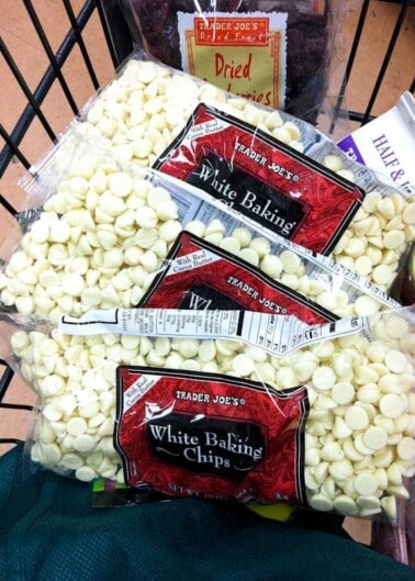 A shopping cart filled with bags of white baking chips and dried fruit from trader joe's.