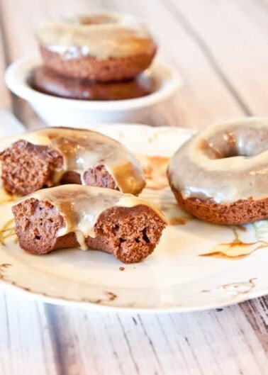 Glazed chocolate donuts on a vintage plate with one donut cut in half to show the inside texture.