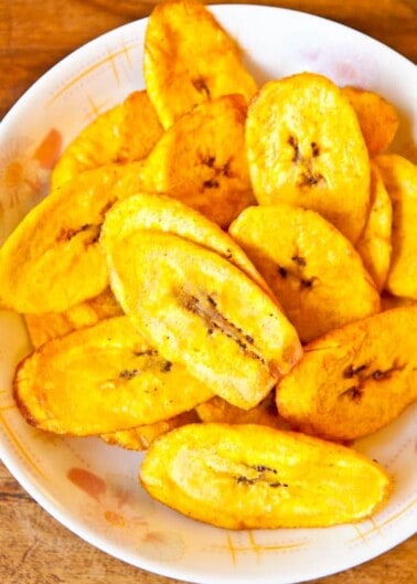 A bowl of fried plantain slices on a wooden table.