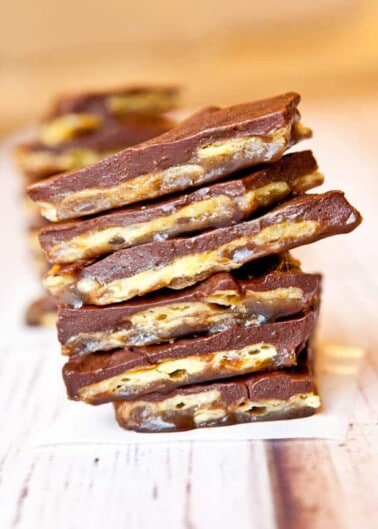 A stack of chocolate-covered toffee bars on a wooden surface.