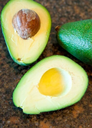 Sliced ripe avocado halves with pit visible on a counter.