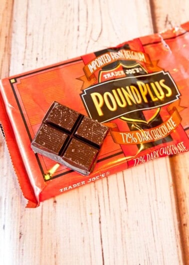 A bar of 72% dark chocolate partially unwrapped on a wooden surface, labeled "trader joe's pound plus.