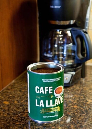 A can of café la llave espresso in front of a coffee maker on a kitchen counter.