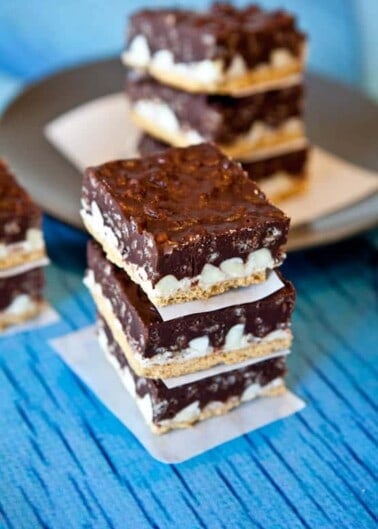 A stack of chocolate-topped dessert bars on a blue wooden surface.