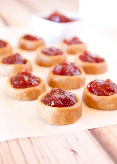 A row of thumbprint cookies filled with jam on a wooden surface.