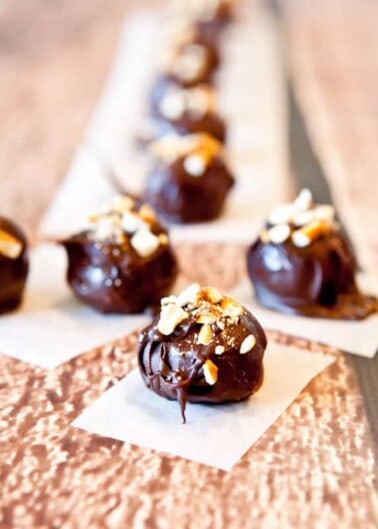 A row of chocolate truffles topped with chopped nuts on a textured surface.