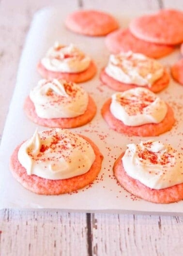 Pink cookies with a dollop of cream cheese frosting and sprinkled with red sugar.