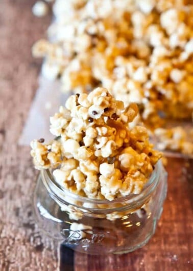A jar filled with caramel popcorn on a wooden surface.