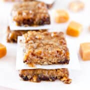 Homemade caramel oat bars on a white surface with scattered caramel candies in the background.