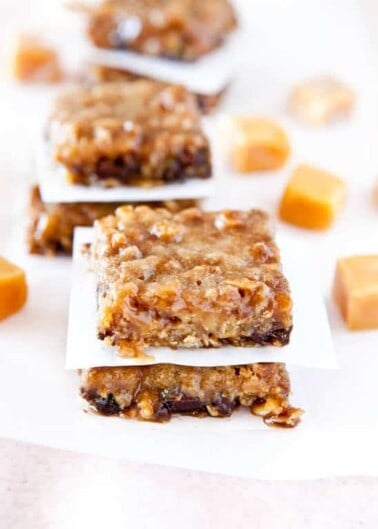 Homemade caramel oat bars on a white surface with scattered caramel candies in the background.