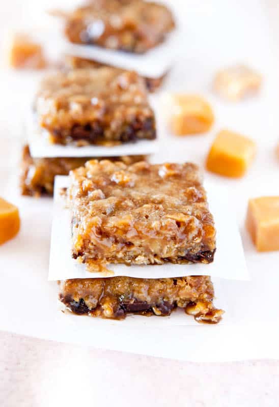 Stacked Caramel and Chocolate Gooey Bars separated by parchment paper