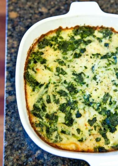 A baked spinach and cheese casserole in a white oval dish.